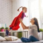 Mother holding up daughter dressed as super hero in bedroom