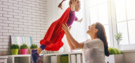 Mother holding up daughter dressed as super hero in bedroom